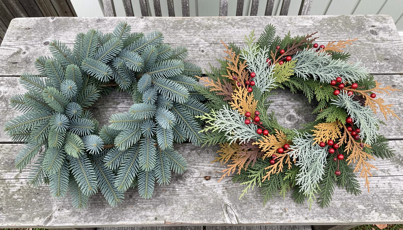 A narrow workbench under a window, a chipped porcelain figure resting on a folded cloth beside a spool of narrow ribbon and a fresh evergreen wreath lying flat, morning light from the left, close framing on the hands and the piece.
